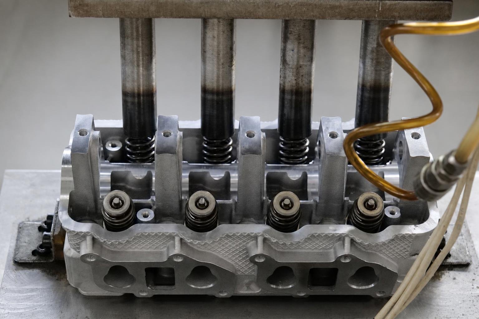 Crisp close-up of a metallic cylinder head, valve springs, and machined surfaces inside an industrial workshop.