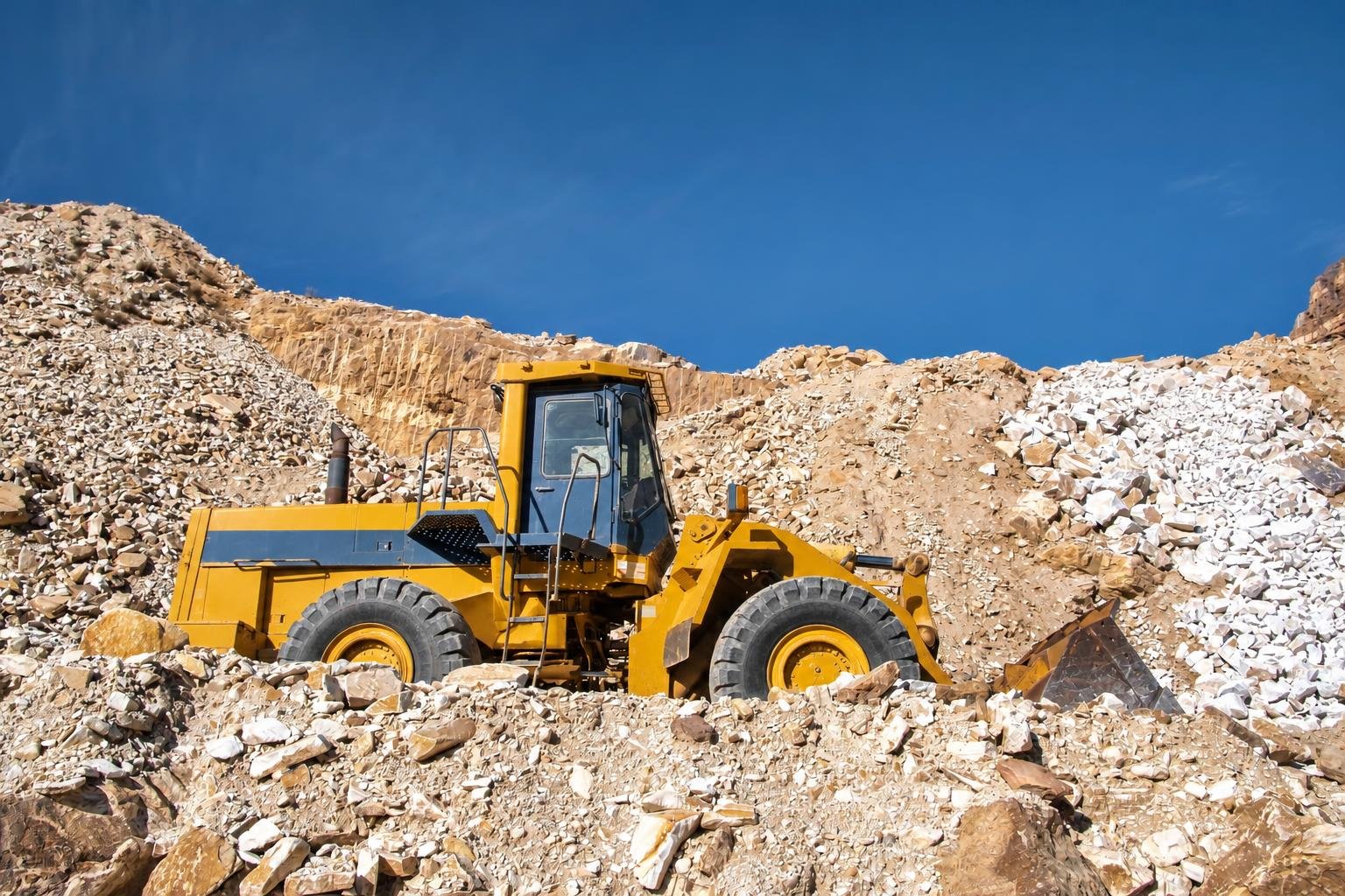 An industrial bulldozer works a large quarry floor surrounded by raw stone and blue sky.