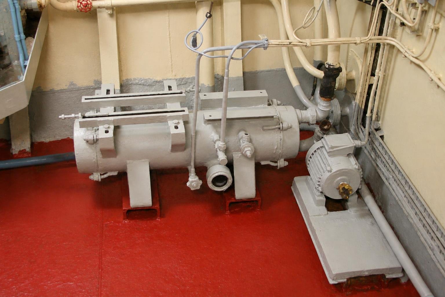 Bank of pumps, valves and pipework inside the working-space engine room of a trawler.