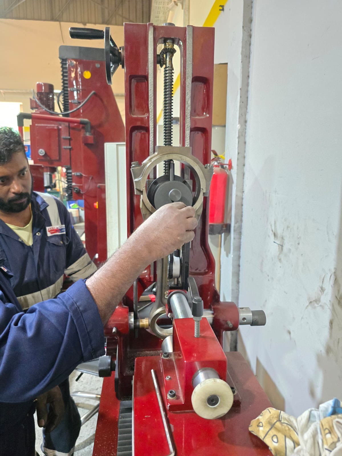 Technician checking a connecting rod on precision workshop equipment.